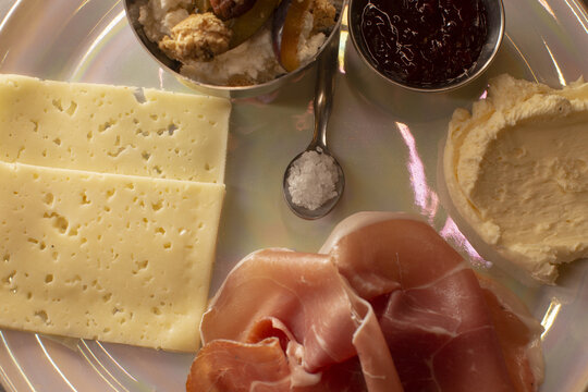 Cheese and prosciutto plate showcasing marinated mushrooms, jam, salt and creamy hummus, arranged on white plate under warm bistro lighting, intimate cafe appetizer perfect for sharing. - Powered by Adobe