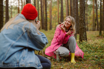 Fototapeta premium Two friends share a cheerful moment in a vibrant forest, dressed in playful outfits. Laughter fills the air as one captures the other’s joyful expression among the trees.