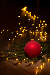 Red glass Christmas ball resting on pine branches with warm golden bokeh lights in the background. Perfect for New Year greetings.