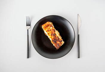 A piece of cheesecake lies on a black plate on a white background, top view