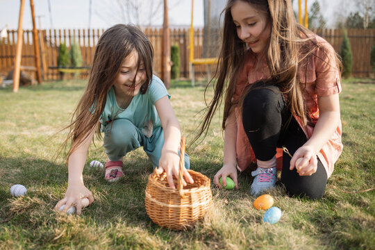 spring fun - finding eggs for easter outdoor in countryside. Happy children sitting on grass with found eggs and put them in a basket on sunny day. easter hunt in backyard.