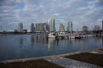 Obraz premium Coastal City Waterfront With Modern Buildings And Calm Vinoy Basin Under Cloudy Sky from the Pier in St. Pete, FL. Cityscape featuring modern high-rises along the shore, calm water, and a cloudy sky, 