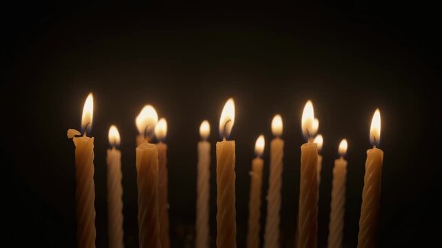Many thin church candles burning with bright flames on a black background. Spiritual vigil, prayer, or memorial concept for religious holidays or remembrance events