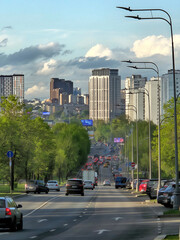 Fototapeta premium Busy city street with cars and a tall building in the background. There are also street lights and a few trees