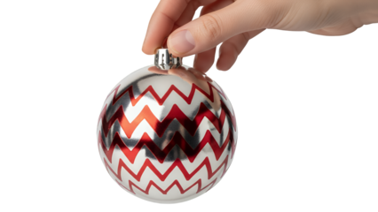 Hand holding a Christmas ornament with red, white, and black zigzag pattern isolated on transparent background