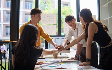 Diverse UX UI design team joining hands together in a creative workspace.