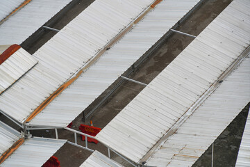High-angle view of many corrugated metal roofs (zinc or tin) overlapping in a dense urban area or traditional market, showing white, grey, and rusty red textures.