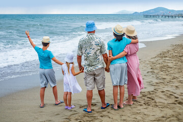 Happy large family standing on sandy beach, looking out ocean waves together, father with mother and children observing waves, family bonding during summer beach holiday getaway, school holidays