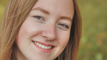 Teenage girl with long brown hair grinning broadly, natural outdoor setting with soft focus background