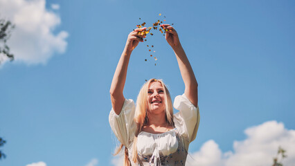 Attractive slavic woman tossing golden confetti, joyfully celebrating with vibrant blue sky backdrop