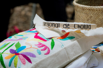 Detail of colorful traditional Mexican embroidery featuring flowers and birds next to a wooden sign identifying it as "Regional de Cholula."