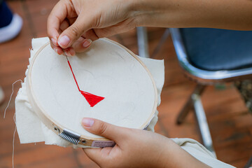 Detailed close-up of artisan hands making precise stitches with red thread on white fabric stretched over a circular embroidery hoop.
