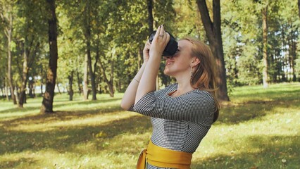 Young photographer taking pictures in a park during a sunny day, surrounded by green trees and grass