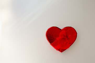 Fototapeta premium Minimalistic shot of red heart shaped gift box on matte gray background with a soft light and copy space