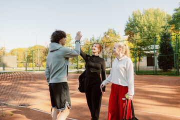 Three friends enjoy a sunny day at the tennis court, sharing high-fives after an exciting match. Their smiles reflect the joy of friendly competition and warm camaraderie.