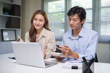 Obraz premium Smiling business team discussing numbers and checking calculations while using a laptop.