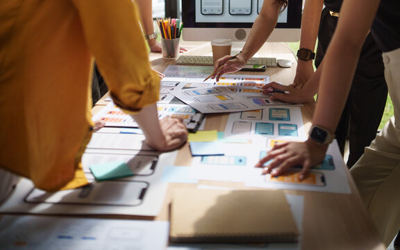 UX UI design team collaborating around a table filled with mobile app wireframes and interface prototypes.