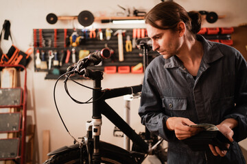 Bike repair and maintenance in workshop. Bicycle mechanic holding open wallet with dollar cash while working on bike repair. people, business, finances and money