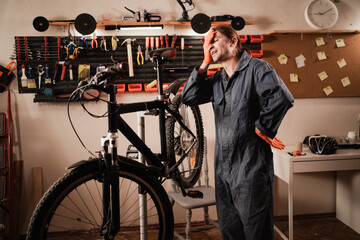 Experienced bicycle mechanic adjusting gear shifter in workshop. In background tools hanging on the wall.