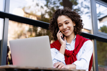 Beautiful cheerful woman remote working, answering call using laptop outdoors