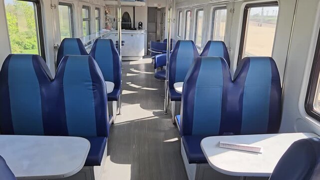 Train with a dining car and bar with blue and white seats and tables is shown. The train is empty, and the interior is clean and well-maintained