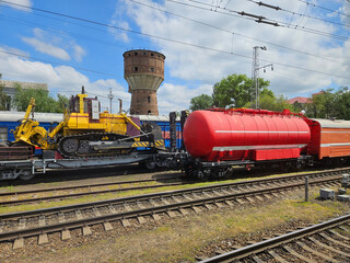 Yellow bulldozer and red train car with a red water tank on top. The train car is on the tracks next to a yellow machine © Pavel Losevsky