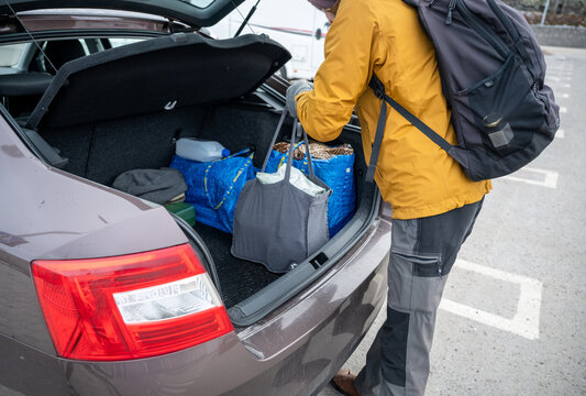 Person unloading reusable shopping bags from car trunk after grocery trip