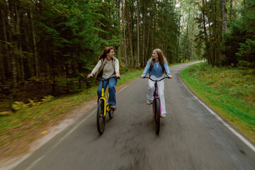 Fototapeta premium Two friends ride their bicycles side by side on a serene forest path. Lush trees surround them, creating a peaceful and joyful atmosphere during a sunny day.