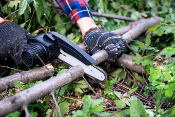 A man in gloves saws a wooden tree trunk with a saw.