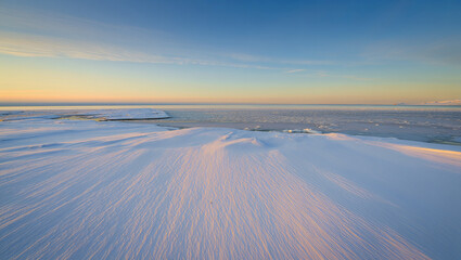 Snow covers the landscape as the sun sets over the ocean and ice