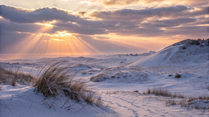 Sunlight shining through clouds over snowy dunes at sunset near the coast in winter season