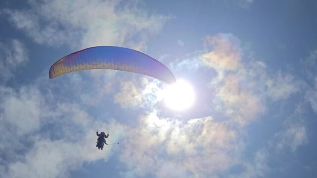 SOCHI - MAY 7, 2025: Man is flying a parachute tandem. The parachute is blue and yellow. The sky is blue and cloudy