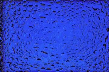 Blue glass surface covered of water drops and condensation, fluid texture. Natural background of moisture, freshness, clarity, abstract reflections in vibrant luminous blue. Trendy electric blue color