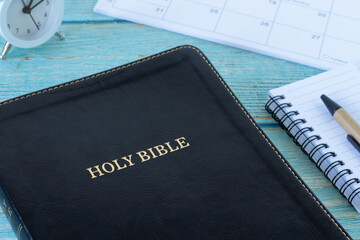Holy bible book with notebook, calendar, and alarm clock. Close-up. Christian scripture study concept, biblical concept.