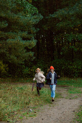Obraz premium Two friends dash along a forest path, their laughter echoing among the trees. With vibrant autumn foliage around, they embrace the excitement of the day.