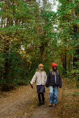 Fototapeta premium Walking hand in hand, two friends enjoy a peaceful day in the colorful autumn woods. The sunlight filters through the trees, creating a warm atmosphere as they explore nature.