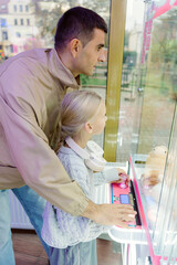 Obraz premium A father and his young daughter enjoy a lively afternoon at an arcade, eagerly trying to win a stuffed toy from the claw machine. Their expressions show excitement and joy.