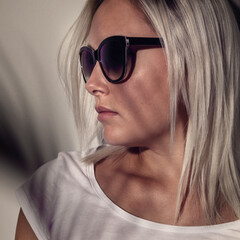 Stylish woman wearing sunglasses with soft shadow overlay on a neutral background