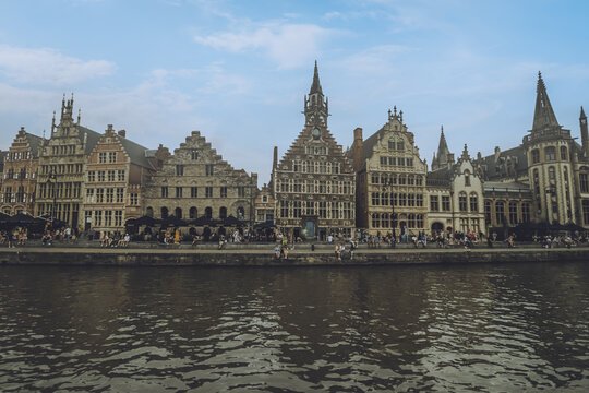 View of ornate guildhalls and gabled roofs line the Graslei waterfront, reflecting in the gentle Leie river under a serene sky, Ghent, Flanders, Belgium.