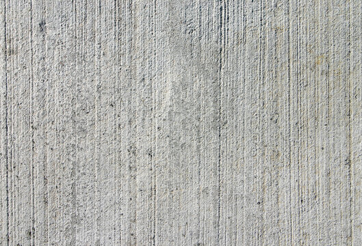 Grooved grey concrete texture. A vertical brushed freshly laid cement surface with industrial details and rough grain.