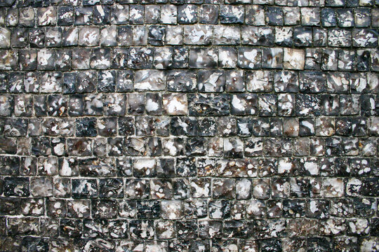 Knapped flint stone wall texture. A traditional masonry background featuring small dark grey and white flint stones in a grid.