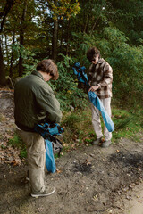 Naklejka premium Two friends are preparing to set up a tent in a serene forest. With trees adorned in vibrant autumn leaves, the scene is peaceful and full of nature's beauty.