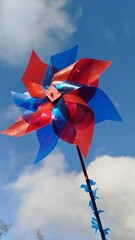 Bright red and blue pinwheel spinning against a blue sky with soft clouds, symbolizing joy, motion, and playful outdoor energy.