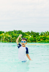 One 7 years old Asian boy splashing water in swimming pool in high end tropical resort