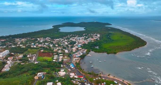 Flight over the cityscape surrounded by the lush greenery. Boats are on the waterscape near the shore of Puerto Rico. Clouds cover the sky over the scenery.