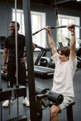 In a spacious gym filled with exercise equipment, two friends share a moment of fitness joy. One...