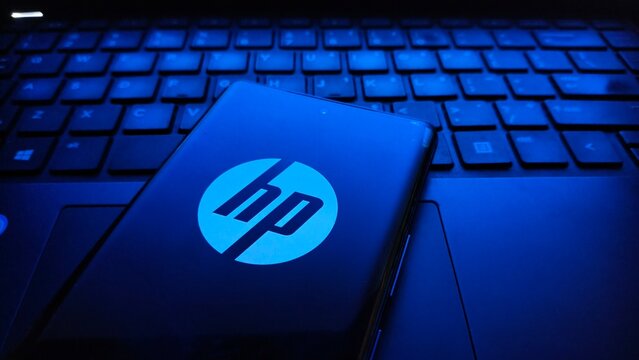Closeup of a smartphone displaying the glowing blue hp logo resting on the backlit keyboard of a laptop in a dark environment, emphasizing technology and branding  , New York City, 15 December 2025