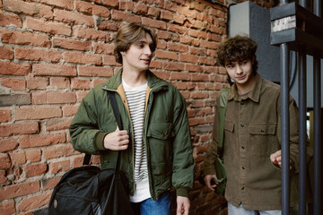 Two young men share a laugh as they enter a stylish, rustic venue with brick walls. Their relaxed outfits and friendly expressions bring a warm atmosphere to the setting.