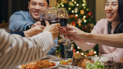 Group of Asia colleague gathering New year holidays party together. Close-up Happy friends group drink glasses of wine start eat christmas dinner at home in evening, celebration and people concept.