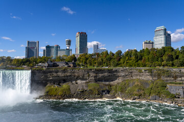 View of Niagara Falls' powerful cascade against the backdrop of the city's skyline, a contrast of nature's raw force and urban development, Niagara Falls, Ontario, Canada.